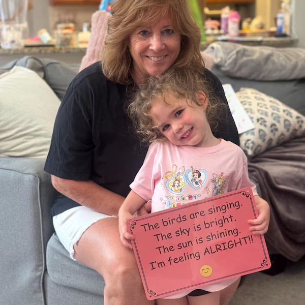 Woman and child holding a pink personalized message sign indoors